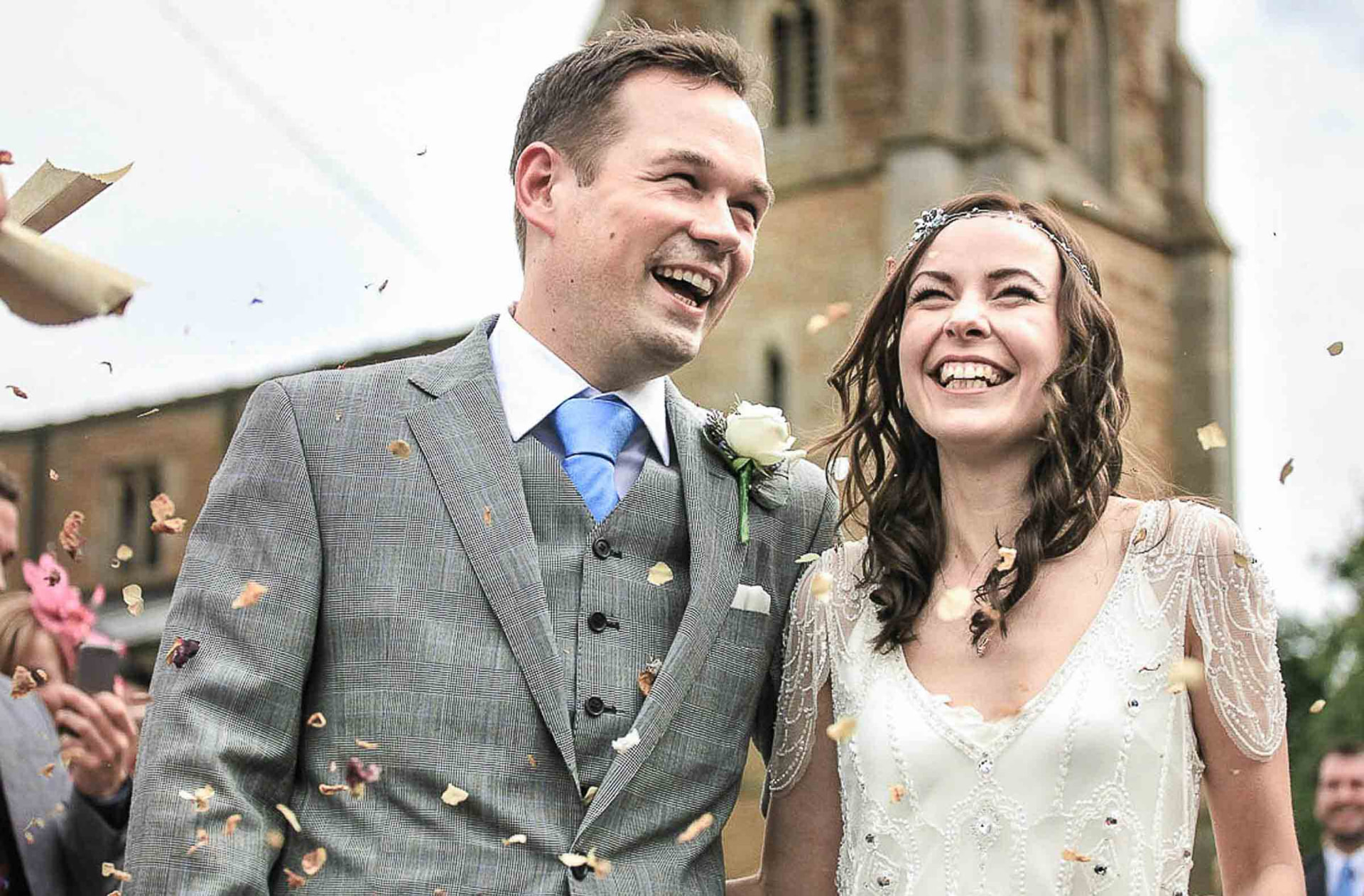 Bride and groom laughing together as confetti falls outside a stone church