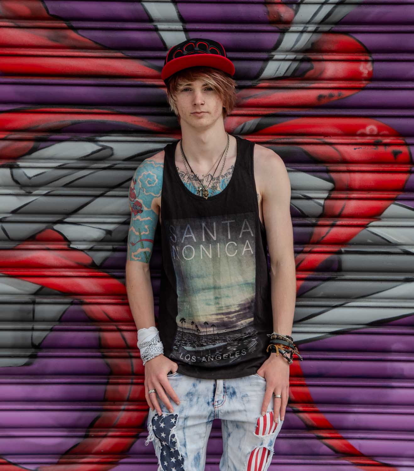 Young man in a snapback cap photographed against a brightly painted graffiti shutter, Newport