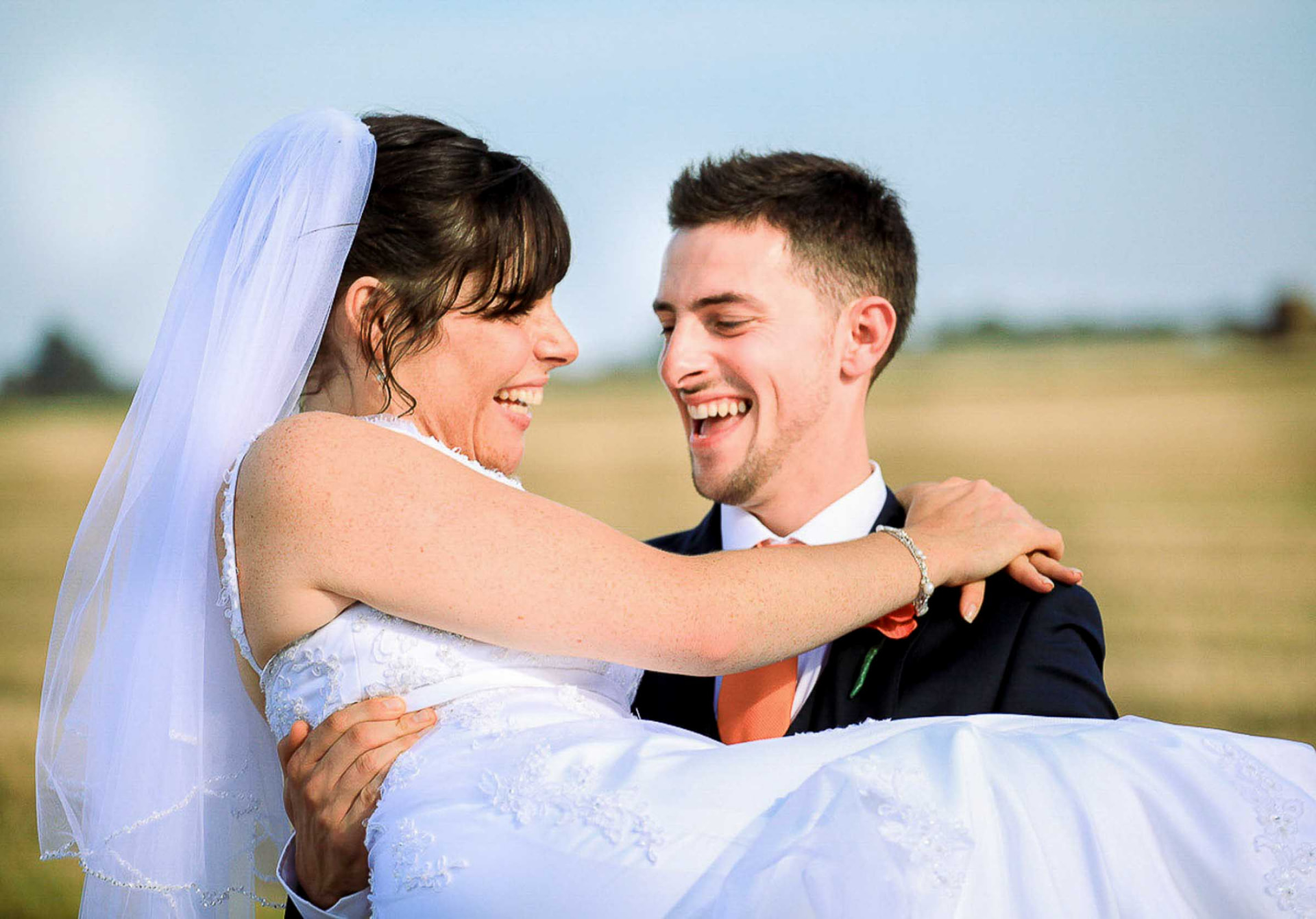 Groom carrying his laughing bride through a sunlit field at a Monmouthshire wedding