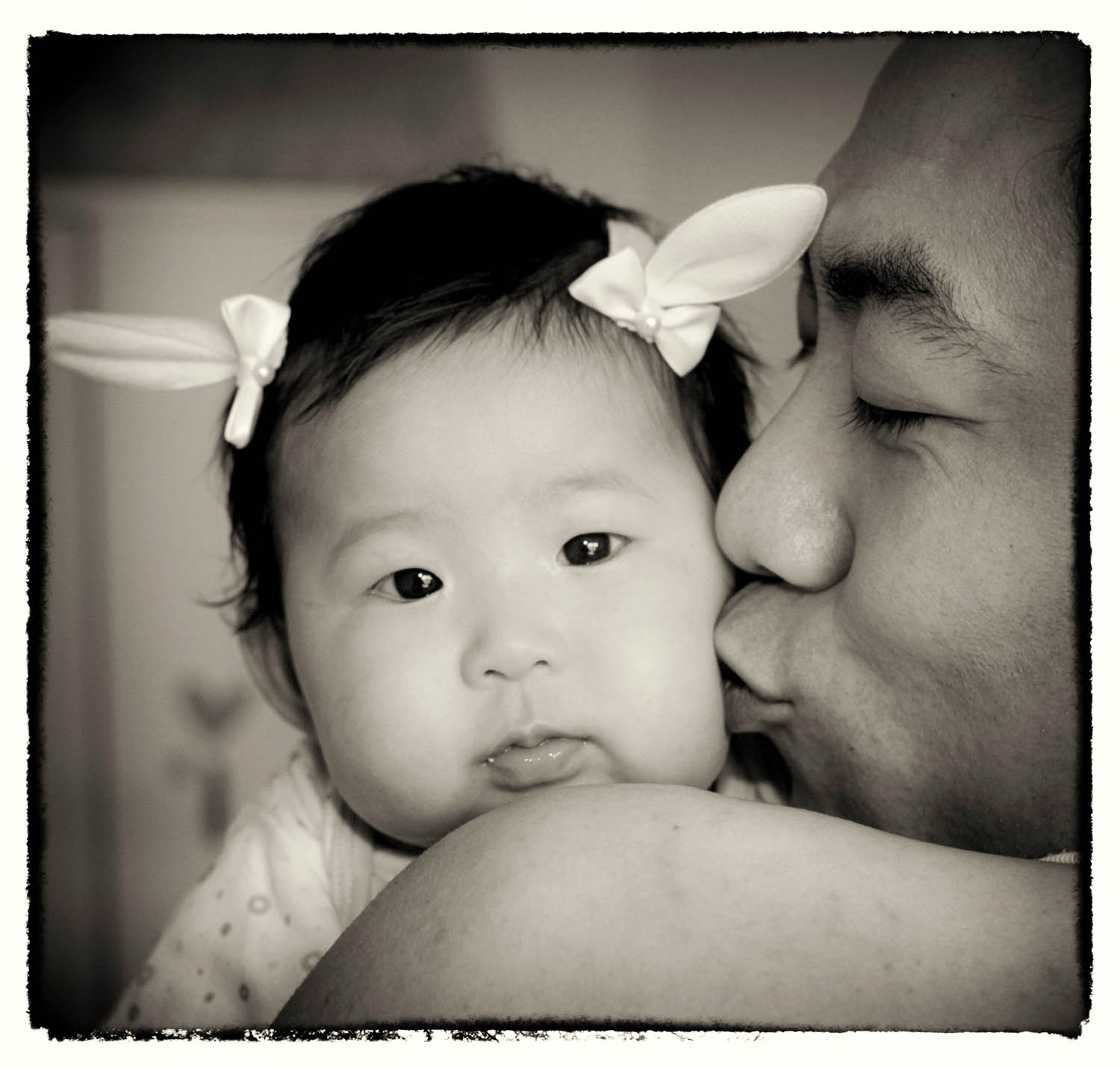 Black and white family portrait of a father kissing his baby daughter on the cheek